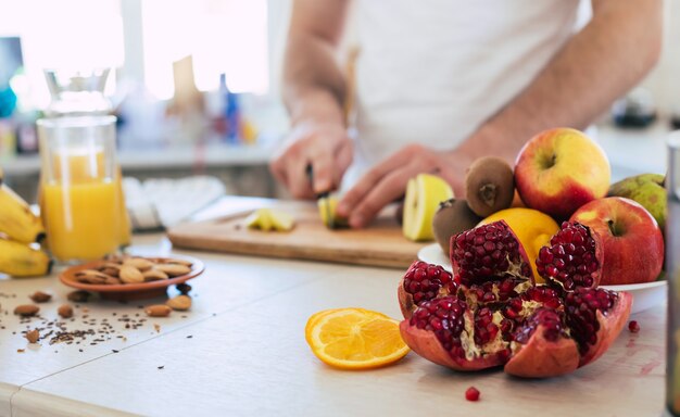 De knappe jonge sportieve glimlachende mens in de keuken hakt fruit