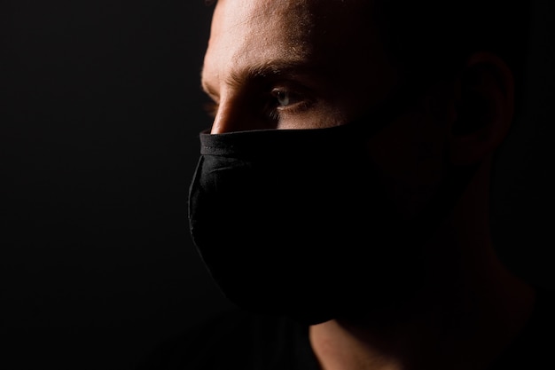 De knappe mens draagt zwart medisch masker tegen coronavirus op grijze achtergrond