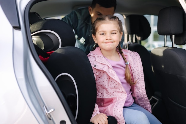 Foto de knappe vader zet haar dochter in een autostoel en sluit haar veiligheidsgordel vast voor bescherming tijdens de reis.