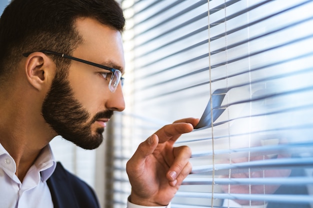 De knappe zakenman die door de blinds kijkt