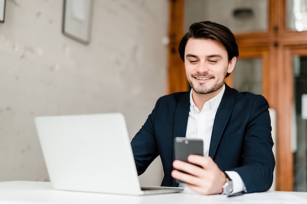 De knappe zakenman in een kostuum gebruikt laptop in het kantoor