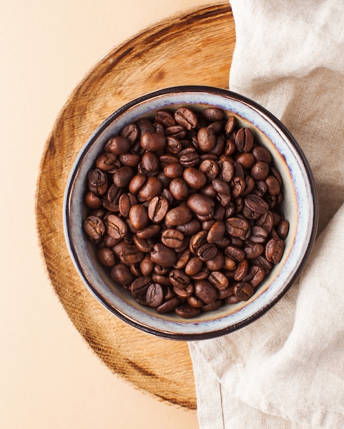 De koffiebonen van arabica in een ceramische kom op een houten dienblad op een bruine achtergrond. verticale foto voor koffiehuizen en coffeeshops.