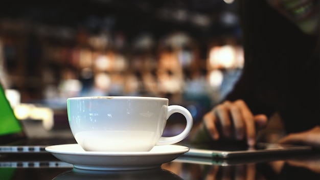 De koffiekoppen van de close-up over de foto vaag van Aziatische vrouw gebruikend de slimme mobiele telefoon