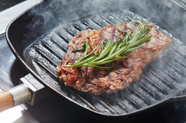 De kok bereidt een vleeslapje vlees op een close-up van de grillpan op een donkere achtergrond voor