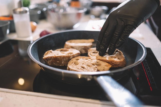 De kok in zwarte rubberen handschoenen haalt de croutons van dichtbij uit de pan