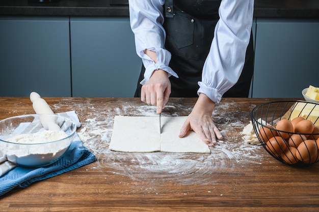 De kok rolt het bakdeeg uit op tafel met de ingrediënten.