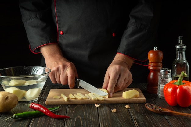 De kok snijdt de aardappelen in kleine stukjes Handen van chef-kok met mes tijdens het bereiden van heerlijk eten