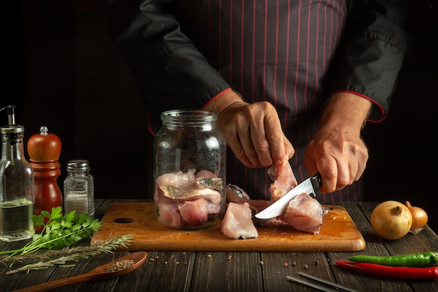 De kok snijdt de vis in steaks voordat hij de haring in een pot bereidt. Werkomgeving op de keukentafel met aromatische specerijen.