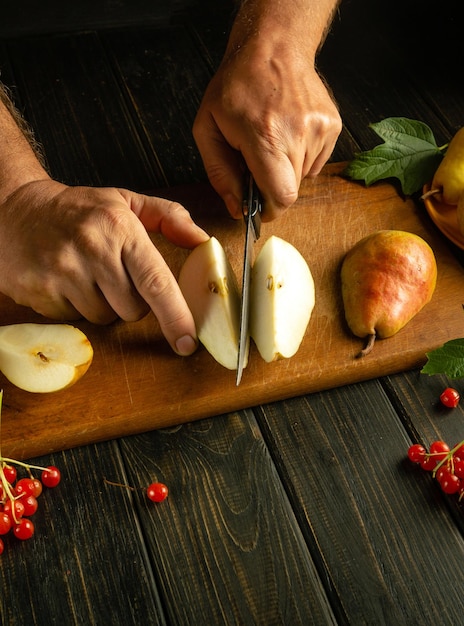 De kok snijdt een rijpe peer op een snijplank om compot of vruchtensap te bereiden.