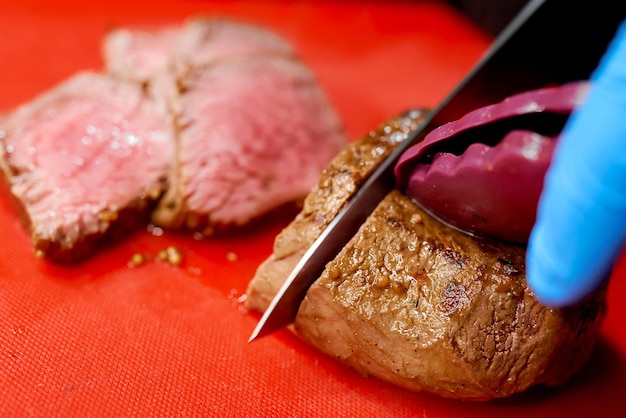 De kok snijdt een sappig gebakken stuk rundvlees met een scherp mes dat zijn hand in een handschoen houdt. Hoge kwaliteit foto