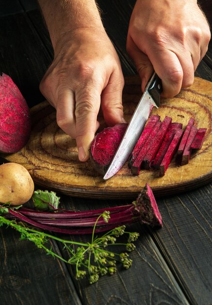 De kok snijdt rode biet of beta vulgaris met een mes om heerlijke borsjt Oekraïense nationale keuken te bereiden