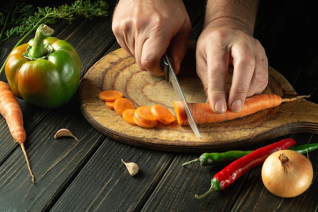 De kok snijdt wortel op een snijplank om ajika te koken