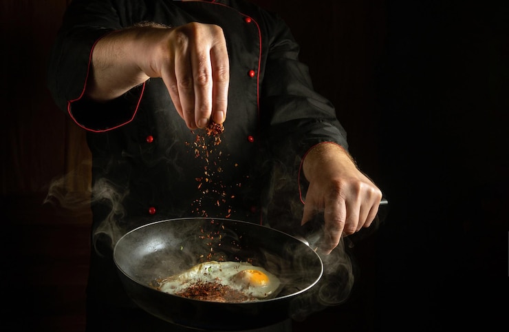 Foto de kok voegt aromatische specerijen toe aan een stoomende hete pan met gebakken eieren