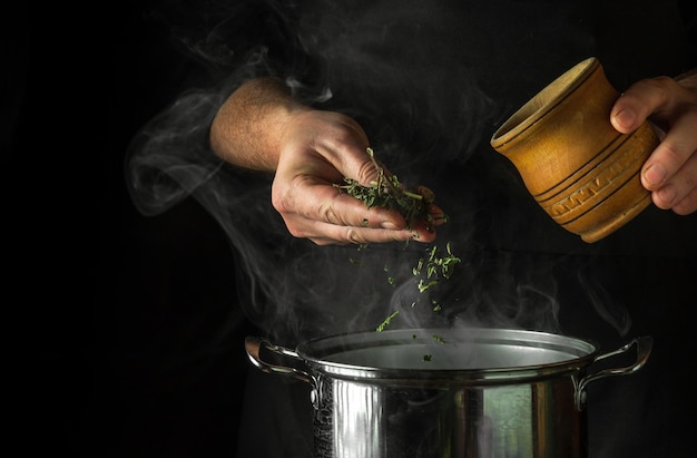 De kok voegt gedroogde kruiden toe aan kokend water in een pot om een vitaminedrankje te maken Idee uit de traditionele geneeskunde met ruimte voor reclame op zwarte achtergrond