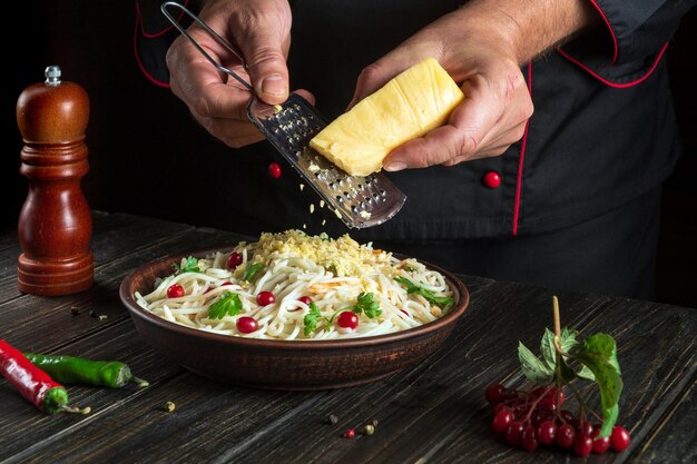 De kok voegt harde kaas toe aan een bord spaghetti Werkomgeving in de hotelkeuken