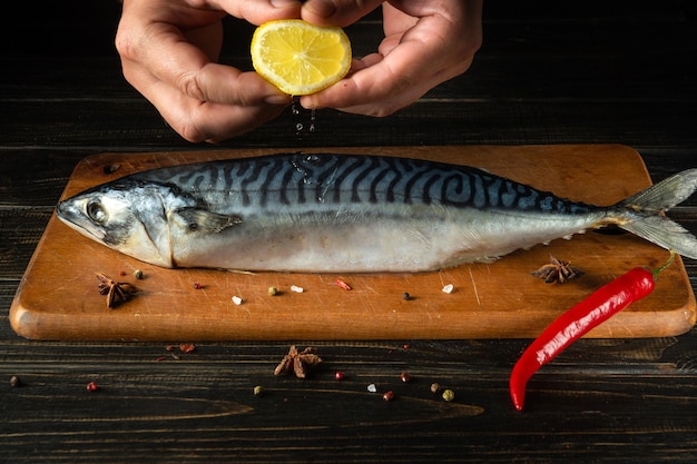 De kok voegt vers citroensap toe aan rauwe makreelvis voordat hij met ingrediënten gaat koken