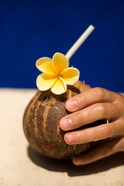 De kokosnotendrank van de handgreep met gele bloem bij poolside