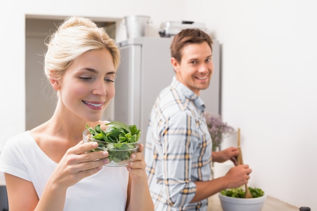 De kom van de vrouwenholding bladeren met de mens die salade op achtergrond in keuken voorbereiden