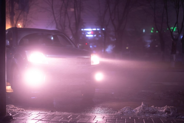 De koplampen van de auto door de mist, slechte en gevaarlijke rijomstandigheden, 's nachts in de stad