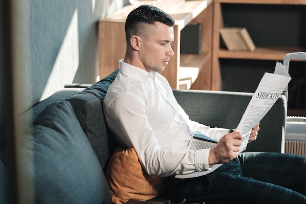 De krant lezen. Jonge knappe zakenman zittend op de bank krant lezen in de ochtend