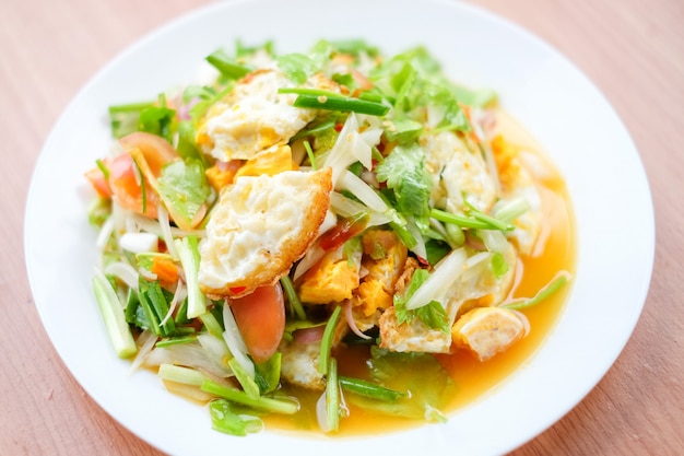 Foto de kruidige salade met gebraden eieren (yam kai dao) dient op witte schotel die op bruine lijst wordt geplaatst - eigengemaakt voedselconcept.