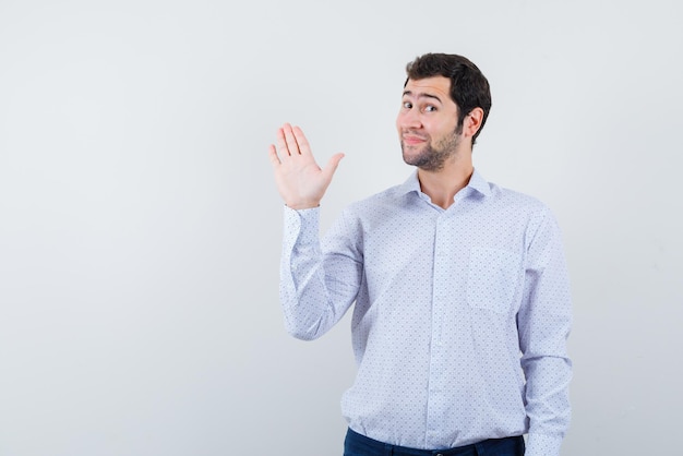 De lachende jonge man zegt "hallo" op een witte achtergrond