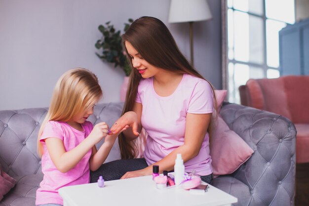 De lachende jonge moeder en haar dochter pronken met hun roze manicure Vrouw en meisje dragen roze kleren en zitten in de kamer