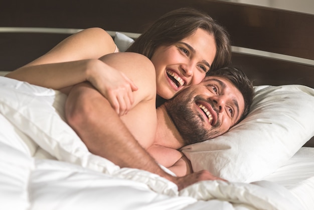 De lachende vrouw knuffelt een man in het comfortabele bed