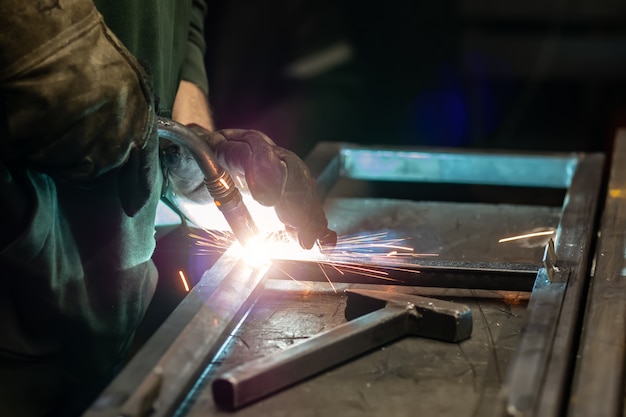 De lasser kookt het frame. De lasser kookt het metaal. De lasser kookt metalen structuren. Lassen werkt. Vonken, gesmolten metaal