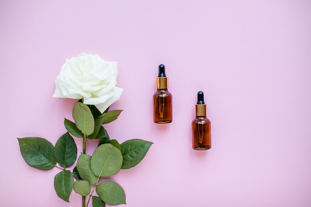 Foto de lay-out van delicate rozen en cosmetische flessenserum op een roze achtergrond