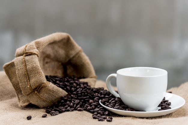 De lege koffiekop en de koffiebonen op de jute hebben klaar omhoog koffie aan de koffie te vullen