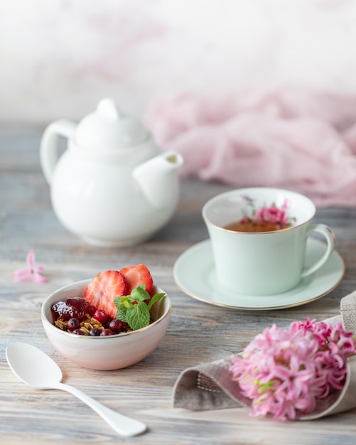 De lenteontbijt met granola en vers aardbeien en litchi en bloemen op houten achtergrond.