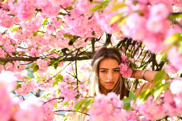 De lentevrouw in de bloei van de kersenbloem. Vrouwendag met meisje in roze kersenbloesem. Sakura bloem schoonheid in de natuur. Huidverzorging en zomer concept. Sensuele vrouw bij tot bloei komende sakurabloem in de lente