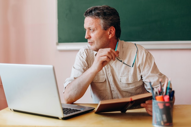 De leraarszitting met handboek en laptop draait zijn hoofd zijwaarts