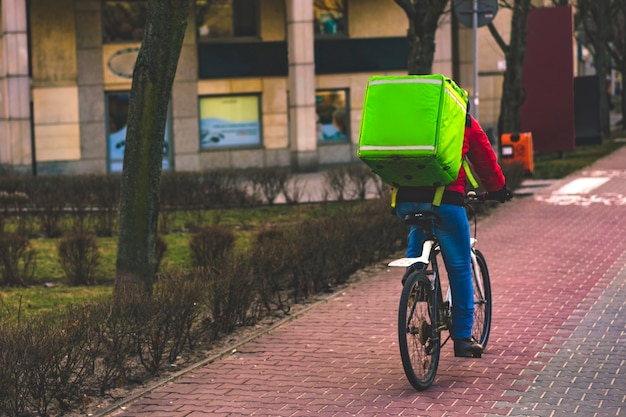 De leveringsbestuurder van het voedsel met groene rugzak op een fiets die langs een weg berijdt