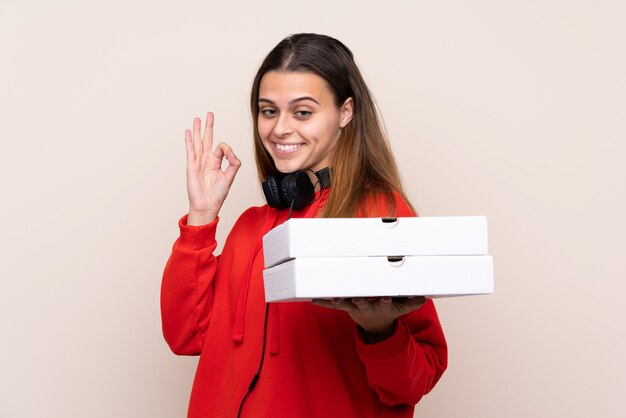 De leveringsmeisje dat van de pizza een pizza over geïsoleerde muur houdt die ok teken met vingers toont