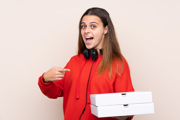 De leveringsmeisje dat van de pizza een pizza over geïsoleerde muur met verrassingsgelaatsuitdrukking houdt