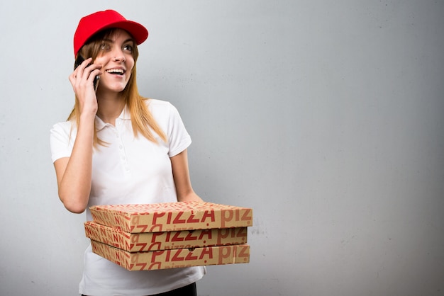 De leveringsvrouw die van de pizza aan mobiel op geweven achtergrond spreekt
