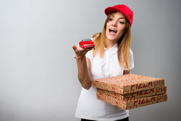 De leveringsvrouw die van de pizza weinig auto op geweven achtergrond houdt