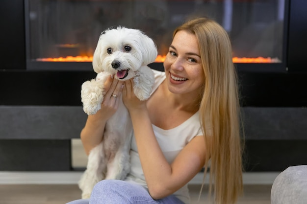 De liefhebbende gastvrouw glimlacht en houdt een pluizige hond in haar armen in de woonkamer van het huis