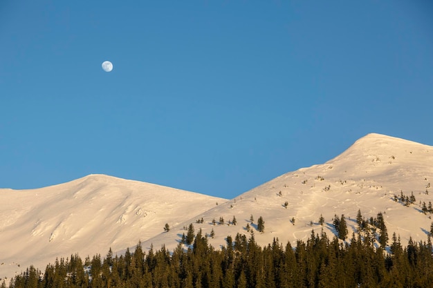 De maan aan de blauwe lucht boven de witte bergtoppen