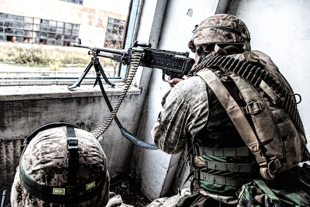 De machinegeweerbemanning van het Korps Mariniers schiet door het raam in een verwoest gebouw tijdens het stadsbrandgevecht. Legermachineschutter valt vijand aan met gericht, direct vuur terwijl zijn kameraad munitieriem vasthoudt