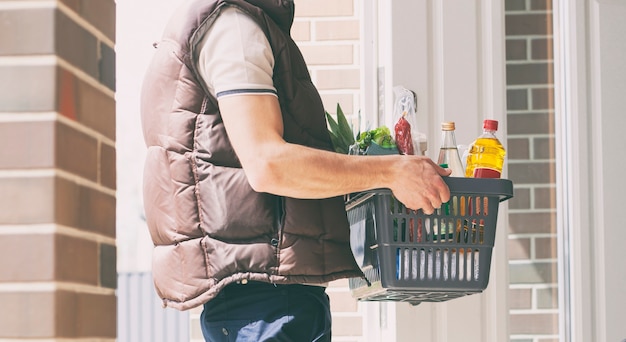 De man bezorgt de mand vol boodschappen aan de deur van het huis. Online winkelen.