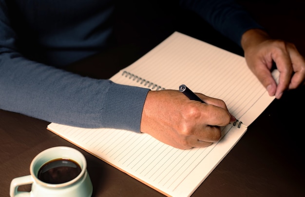 De man die met pen op notitieboek schrijft en zwarte koffie drinkt. Activiteiten op vrije dag