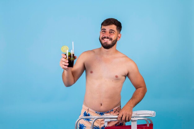 De man die naar het strand gaat, heeft een strandstoel en een drankje in zijn handen