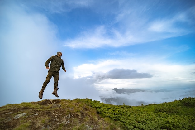 De man die op de berg op de achtergrond van de wolkenhemel springt