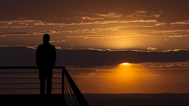 De man die op het balkon staat op de achtergrond van de schilderachtige zonsondergang