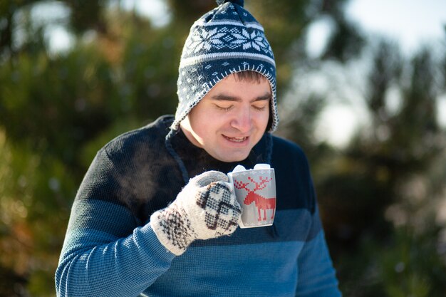 De man drinkt een warme drank met marshmallows in de winter in het bos. Een gezellige winterwandeling door het bos met een warm drankje