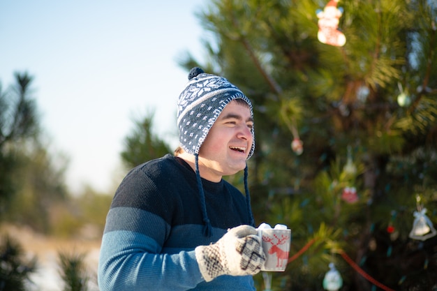 De man drinkt een warme drank met marshmallows in de winter in het bos