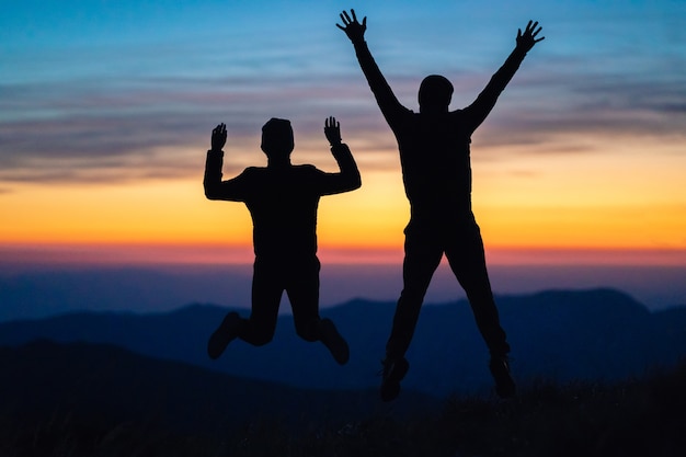 De man en een vrouw die op de berg op de zonsondergangachtergrond springen
